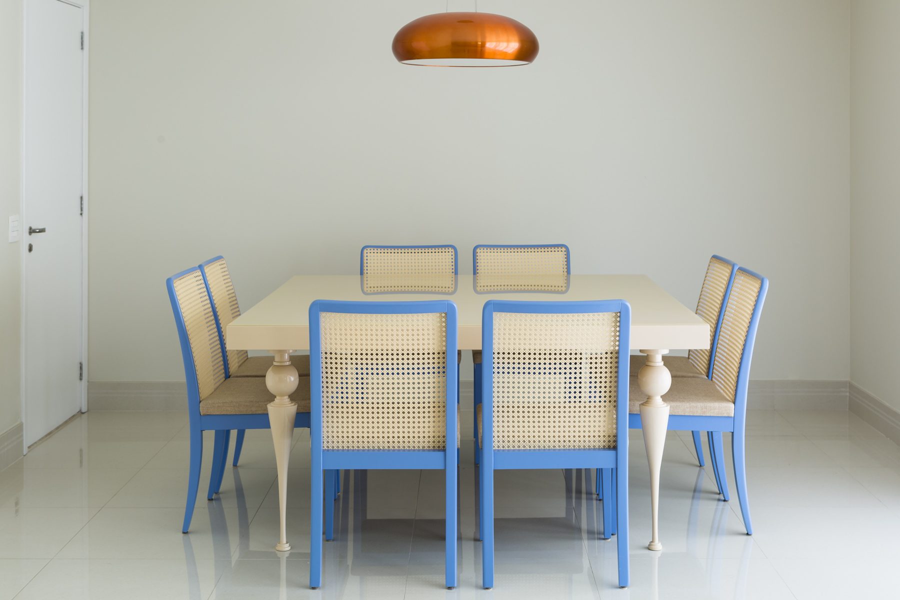 Sala de jantar com cadeiras azuis e pendente de cobre